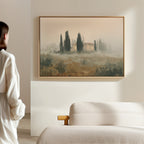 A person in a white robe admires the Tuscan Veil Canvas Art—hung above a beige sofa on a light wall—in a minimal, modern room.