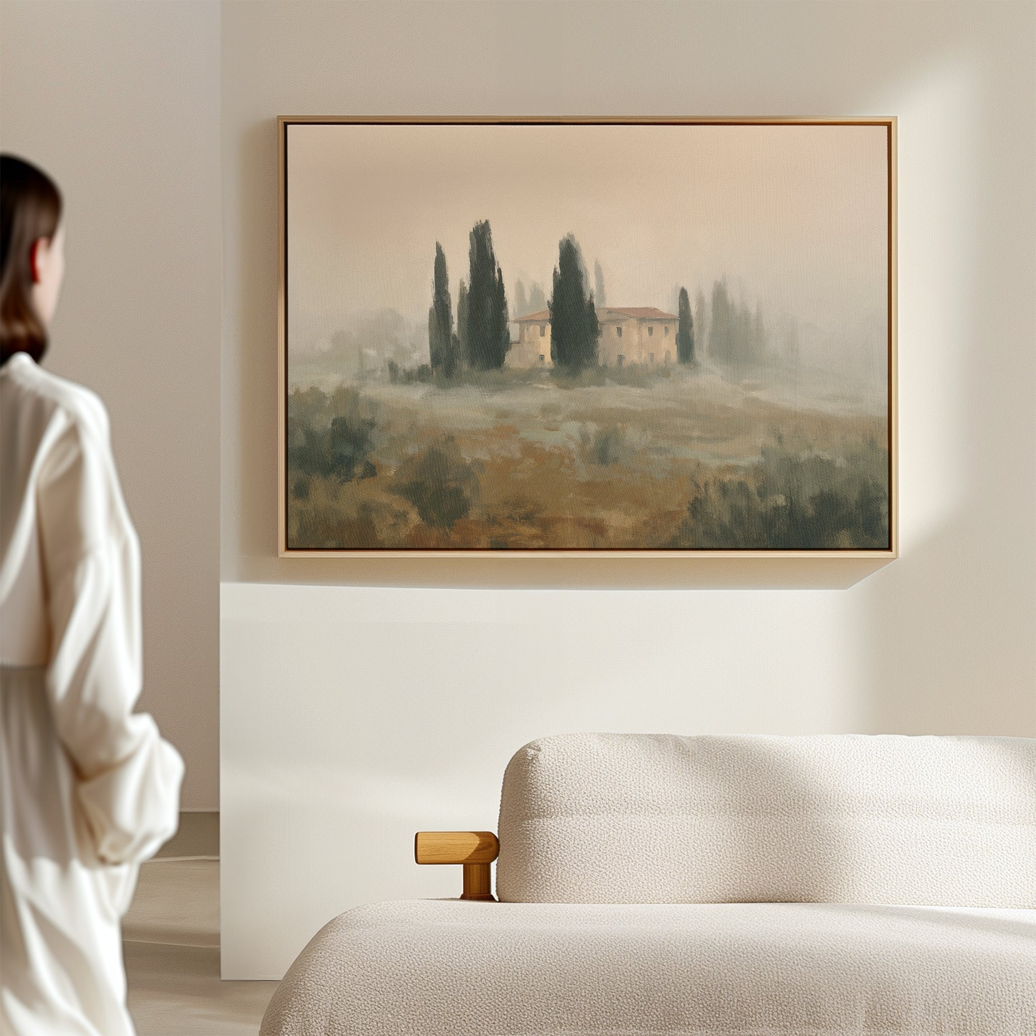 A person in a white robe admires the Tuscan Veil Canvas Art—hung above a beige sofa on a light wall—in a minimal, modern room.