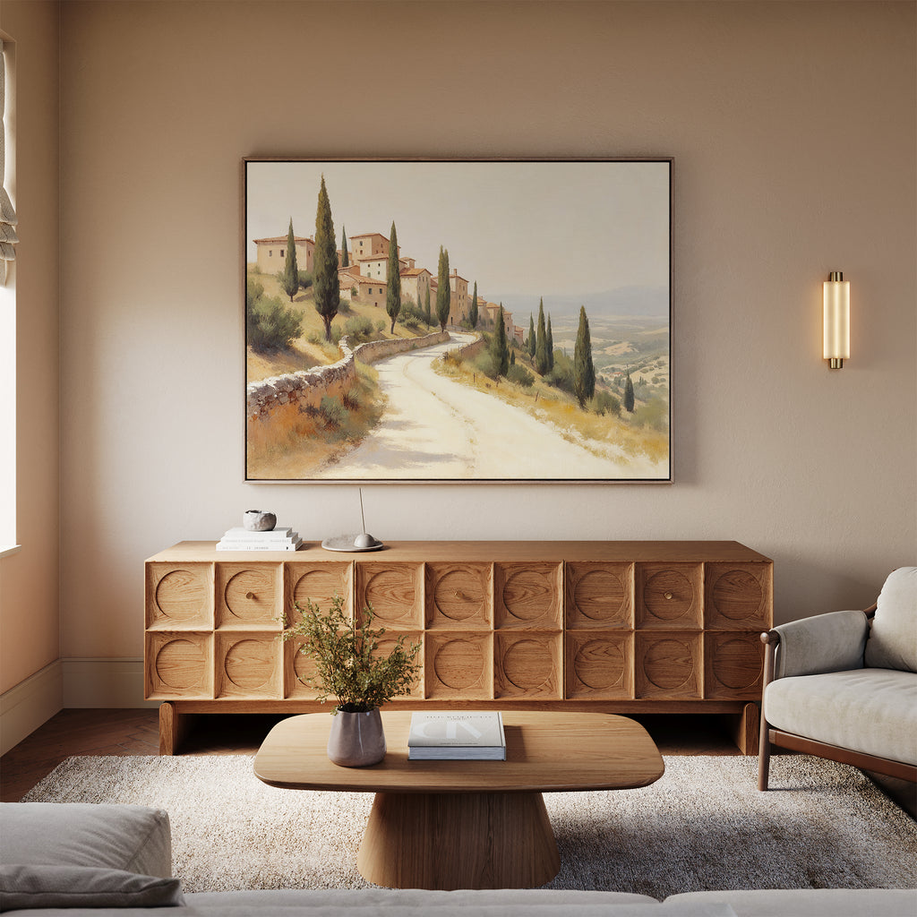A cozy living room with a light sofa, wooden coffee table, textured sideboard, and the Tuscan Village Canvas Art - Horizontal depicting a countryside village. A small vase with flowers rests on the table.