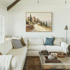 A cozy, bright living room with white shiplap walls, a large white sectional sofa with assorted pillows, a rustic wooden coffee table, and the Tuscan Village Canvas Art - Horizontal hanging above the couch.