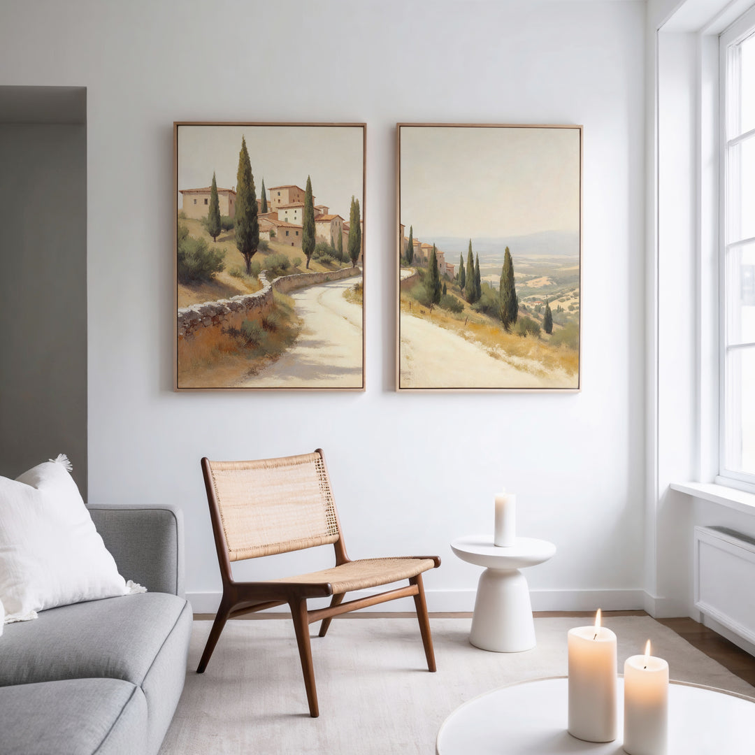 A minimalist living room with a gray sofa, wicker chair, and the Tuscan Village - Set of 2 rustic wall art; candles and natural light enhance the calm, cozy vibe.