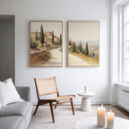 A minimalist living room with a gray sofa, wicker chair, and the Tuscan Village - Set of 2 rustic wall art; candles and natural light enhance the calm, cozy vibe.