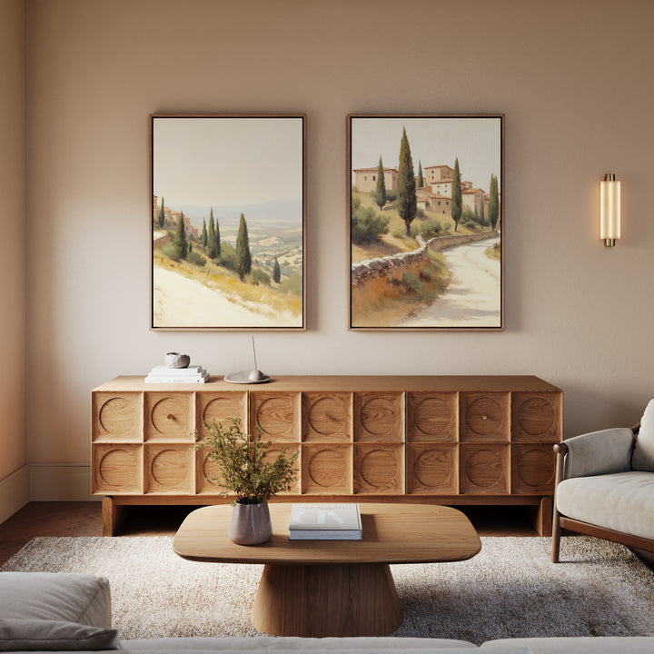 A cozy living room with a wooden coffee table, sideboard, light sofa, and the "Tuscan Village - Set of 2" Mediterranean canvas prints hanging above the sideboard on a beige wall.