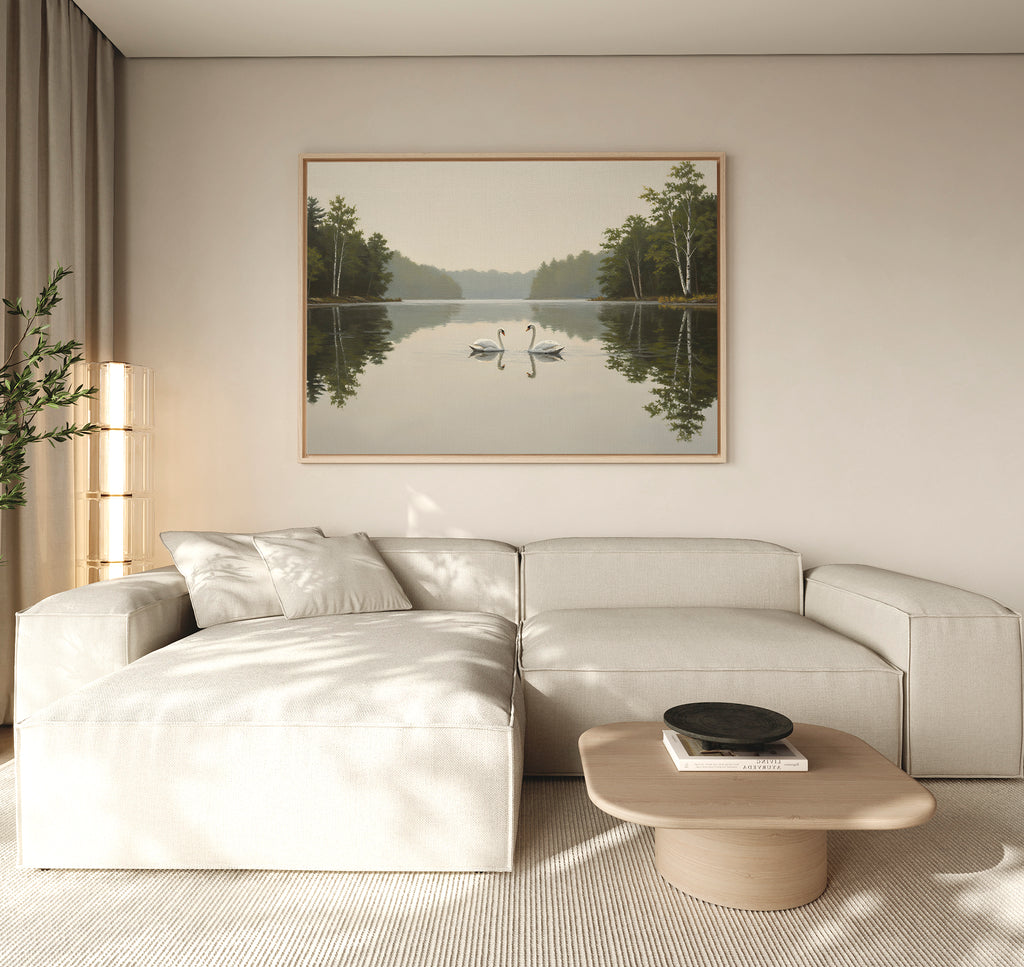 A modern living room with a light beige sectional sofa, a wooden coffee table, and the Twin Swans Serenity Canvas Art - Horizontal: a large framed artwork of two swans on a calm lake with trees, hanging on the wall.