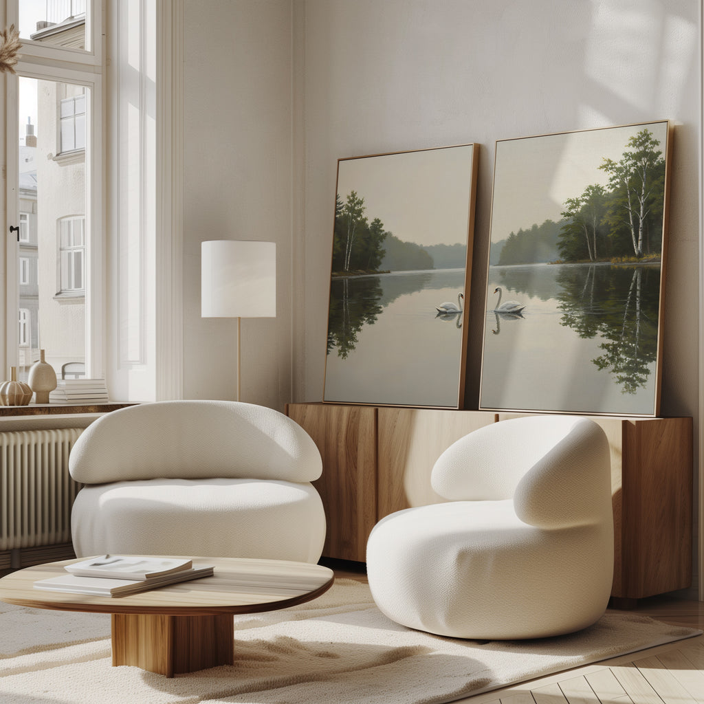 A bright, modern living room with two white, rounded armchairs, a wooden coffee table, and a sideboard. The Twin Swans Serenity - Set Of 2 wall art rests on the sideboard, adding calm and nature-inspired style to Nordic decor.