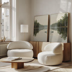 A bright, modern living room with two white, rounded armchairs, a wooden coffee table, and a sideboard. The Twin Swans Serenity - Set Of 2 wall art rests on the sideboard, adding calm and nature-inspired style to Nordic decor.