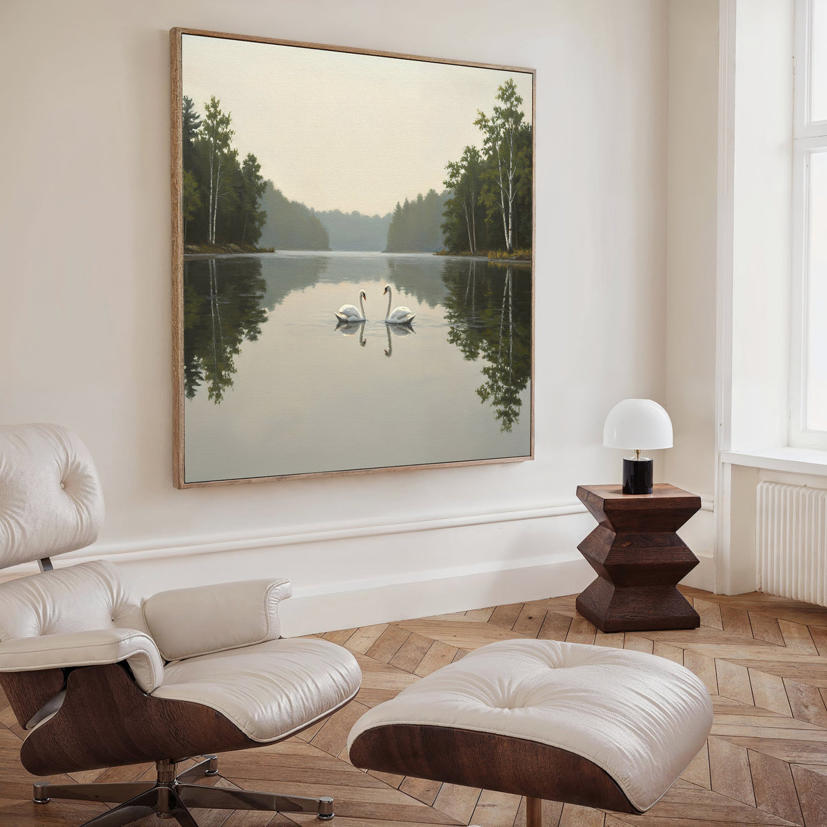 A modern living room with a white lounge chair and ottoman, a wooden side table with lamp, and the Twin Swans Serenity Canvas Art - Square—evoking the peaceful beauty of swans on a Nordic Park lake surrounded by trees.
