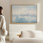 A person in a white top stands in a softly lit room, gazing at the Urban Mirage Canvas Art - Horizontal—an abstract city skyline print above a beige textured sofa—elevating the modern living room decor.