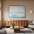 A modern living room with a light wood coffee table, textured sideboard, beige couch, soft lighting, and a vase of flowers is finished with the Urban Mirage Canvas Art - Horizontal for a stylish city skyline decor touch.