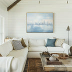 A cozy living room with white shiplap walls, a white sectional sofa, assorted pillows, a rustic wooden coffee table, and the Urban Mirage Canvas Art - Horizontal—a striking city skyline print—hanging above the sofa.