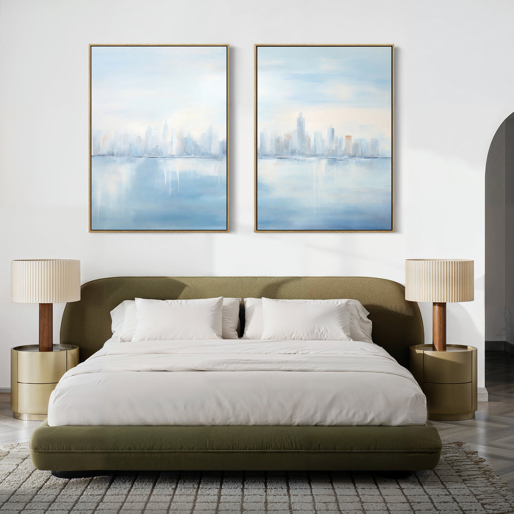 A modern bedroom with a low olive-green upholstered bed, white bedding, beige round nightstands with matching lamps, and the Urban Mirage - Set of 2 canvas city skyline prints displayed above the bed.