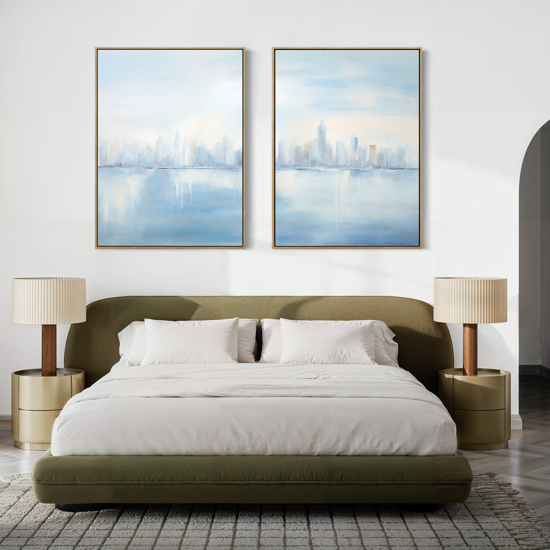 A modern bedroom with a low olive-green upholstered bed, white bedding, beige round nightstands with matching lamps, and the Urban Mirage - Set of 2 canvas city skyline prints displayed above the bed.