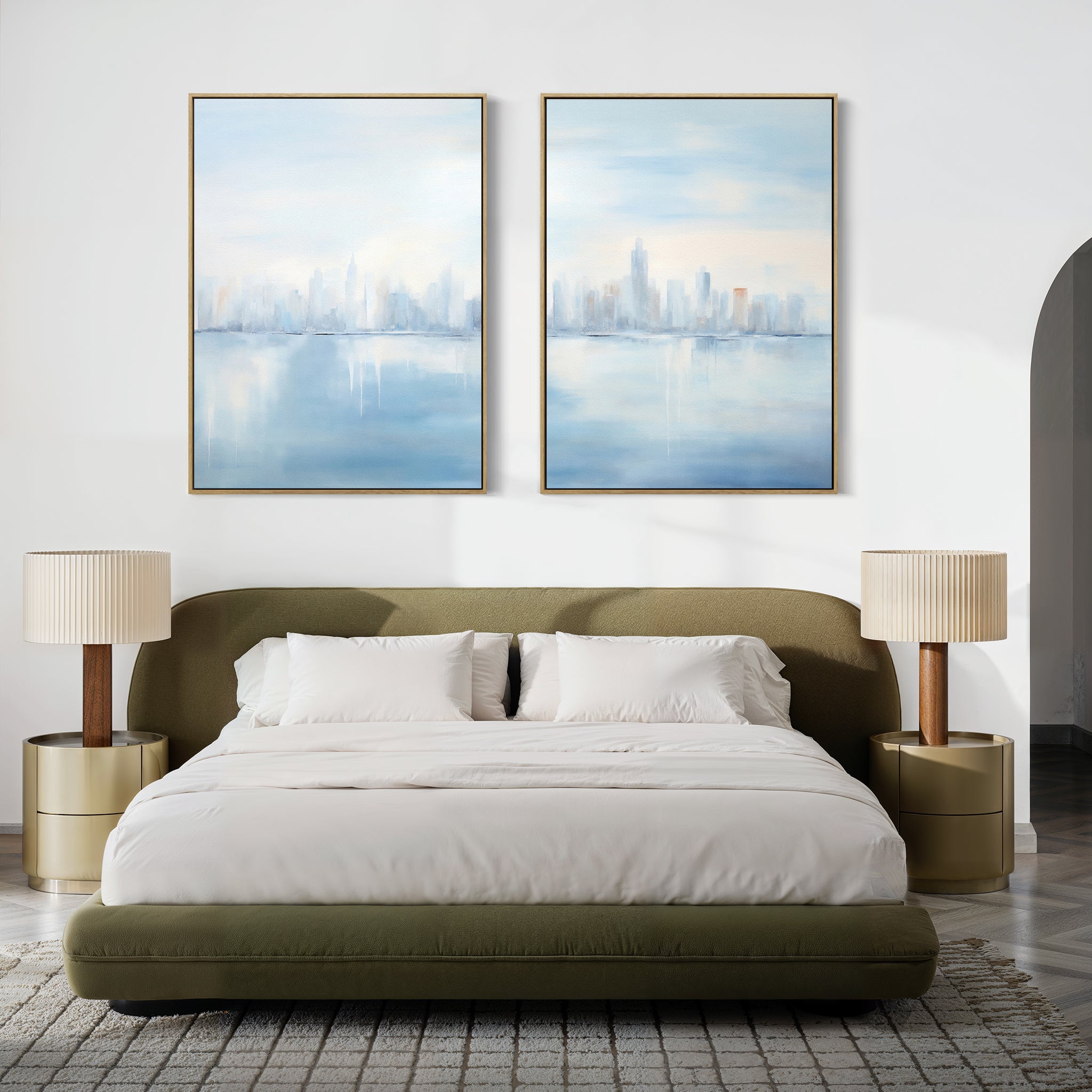 A modern bedroom with a low olive-green upholstered bed, white bedding, beige round nightstands with matching lamps, and the Urban Mirage - Set of 2 canvas city skyline prints displayed above the bed.