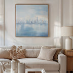 A modern living room with a light beige sofa, neutral pillows, a side table topped with a cream lamp, and vases of dried flowers. Above the sofa hangs the Urban Mirage Canvas Art - Square, adding striking modern cityscape wall decor.