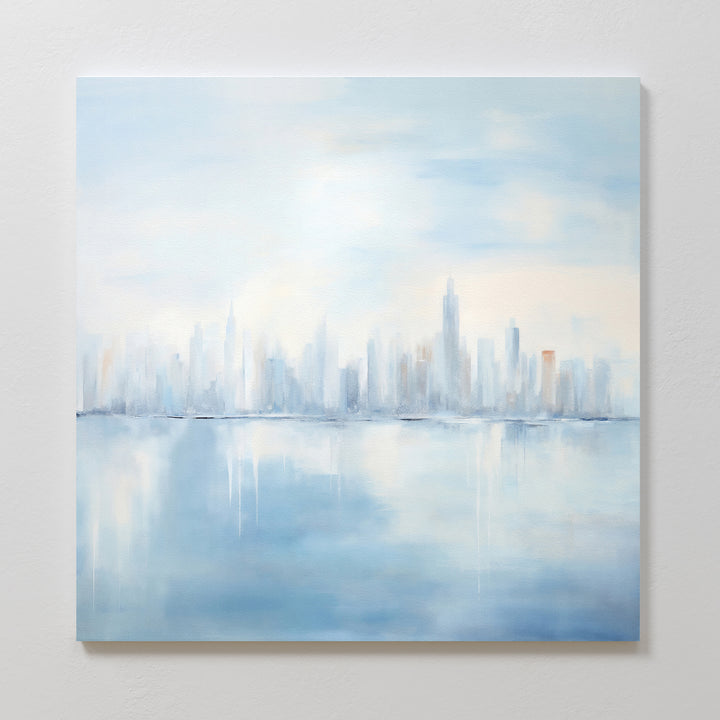 Urban Mirage Canvas Art - Square features a dreamy, abstract city skyline with tall buildings reflected in calm water. Soft blue and gray hues create a serene mood, making it ideal modern wall decor for your living room.