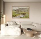 Modern living room with a light beige sectional sofa, wooden coffee table, potted plant, and the Valley Stream Canvas Art - Horizontal above the couch, adding natural countryside beauty with its river and hills landscape.