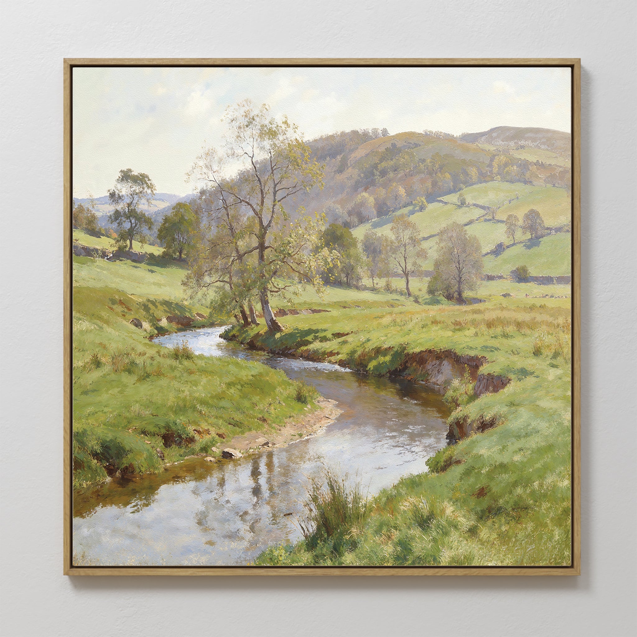The Valley Stream Canvas Art - Square showcases a framed countryside landscape with a winding river, grassy fields, scattered trees, rolling hills, and a partly cloudy sky.