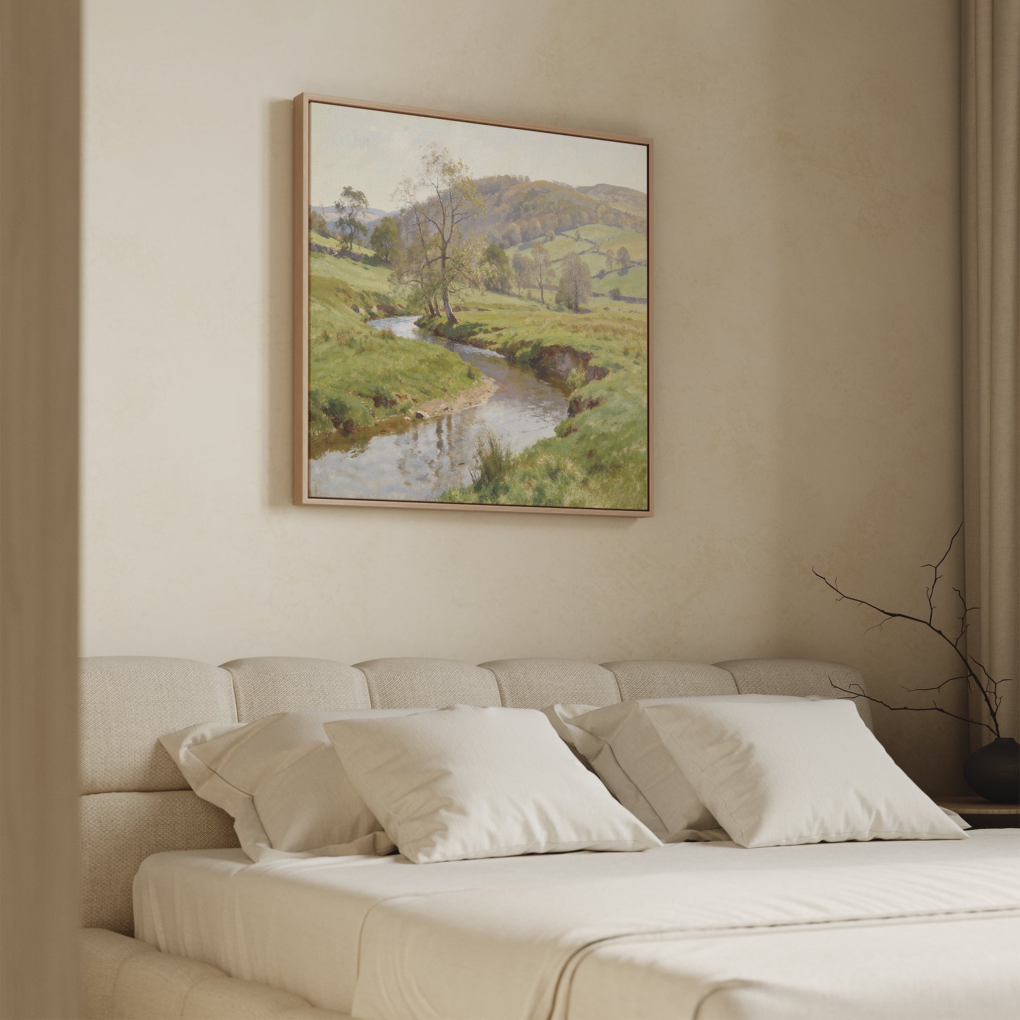 A cozy bedroom with a beige upholstered bed, four white pillows, light bedding, and the Valley Stream Canvas Art - Square featuring a serene green countryside with a river and hills hanging above the headboard.