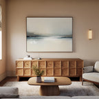 A modern living room with a light beige sofa, wooden coffee table, textured sideboard, minimalist decor, soft lighting, and the Veiled Estuary Canvas Art - Horizontal on the wall creates a calm, cozy atmosphere.