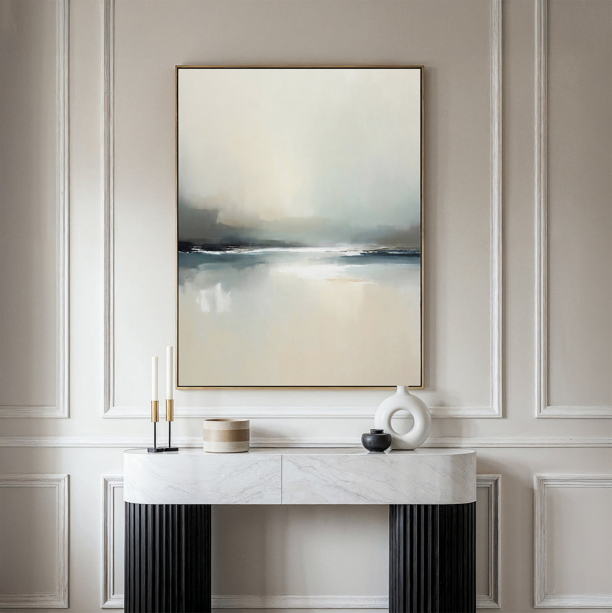 A modern console table displays decorative objects against a wall with elegant molding. Above hangs the Veiled Estuary Canvas Art - Vertical, its soft white, gray, and blue tones evoking the tranquil beauty of a Nordic landscape.
