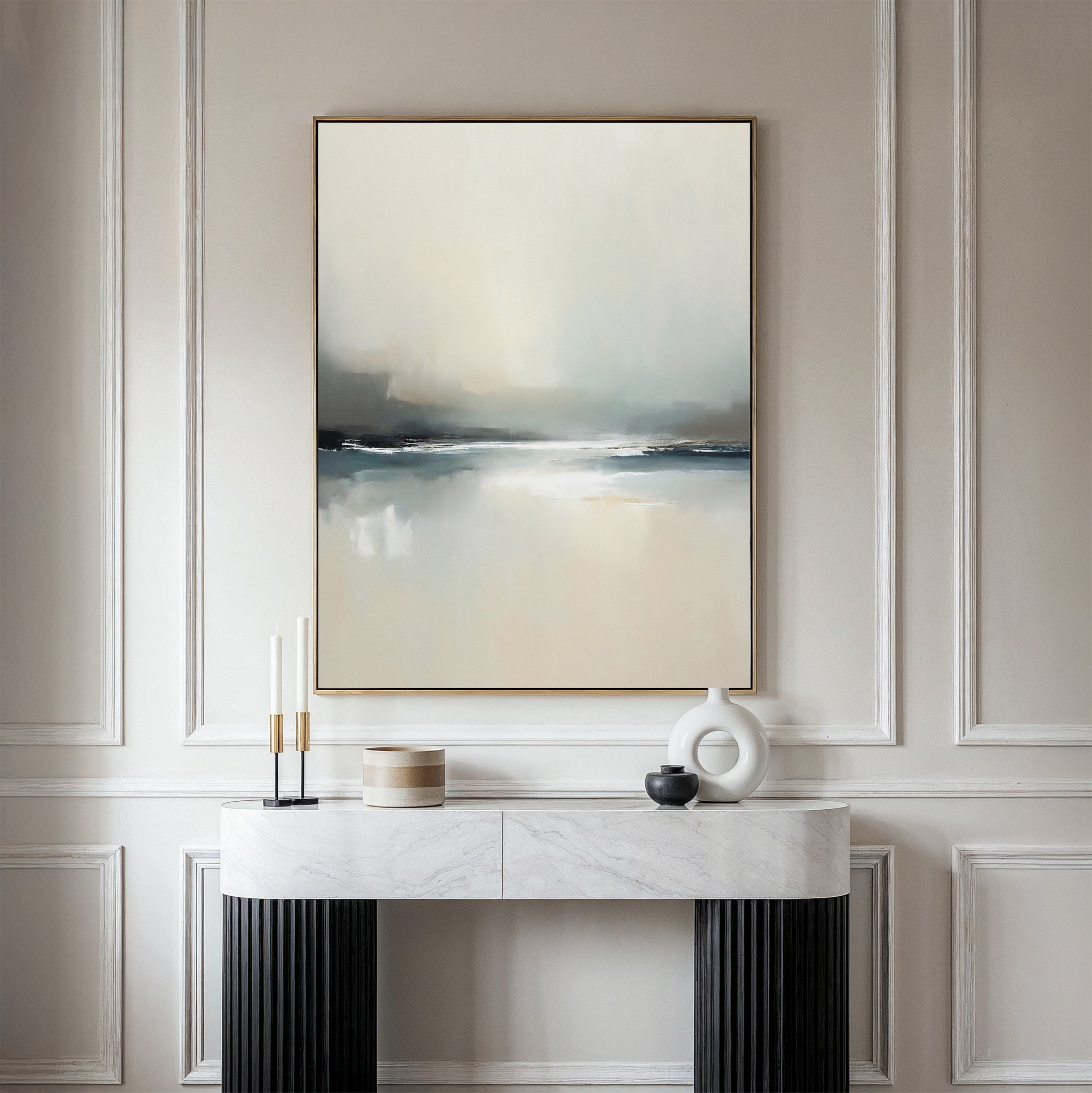 A modern console table displays decorative objects against a wall with elegant molding. Above hangs the Veiled Estuary Canvas Art - Vertical, its soft white, gray, and blue tones evoking the tranquil beauty of a Nordic landscape.