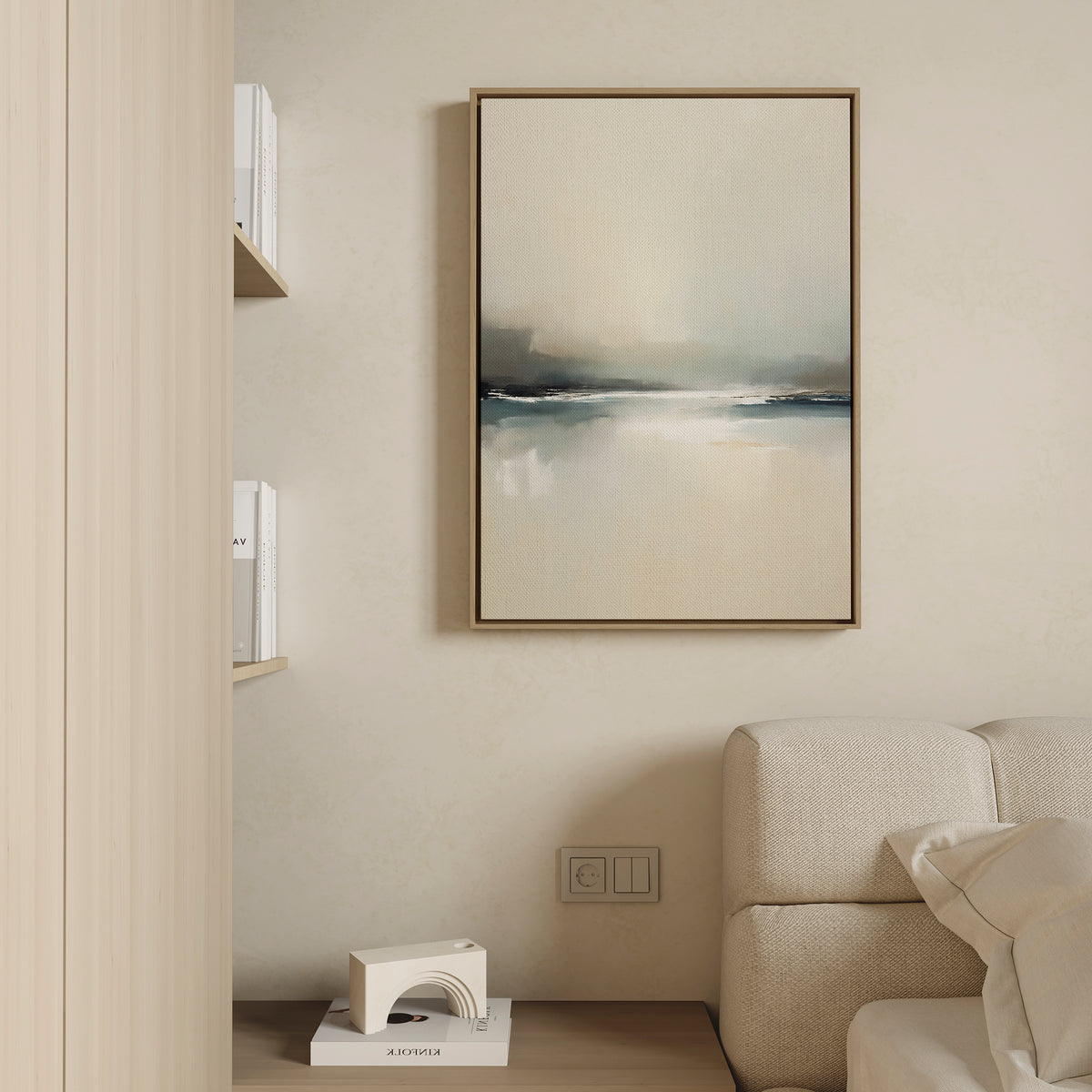 A minimalist living space features a beige sofa, light wood shelves with white books, and Veiled Estuary Canvas Art - Vertical—an abstract painting in soft blue, gray, and beige—enhancing the cream-colored wall.