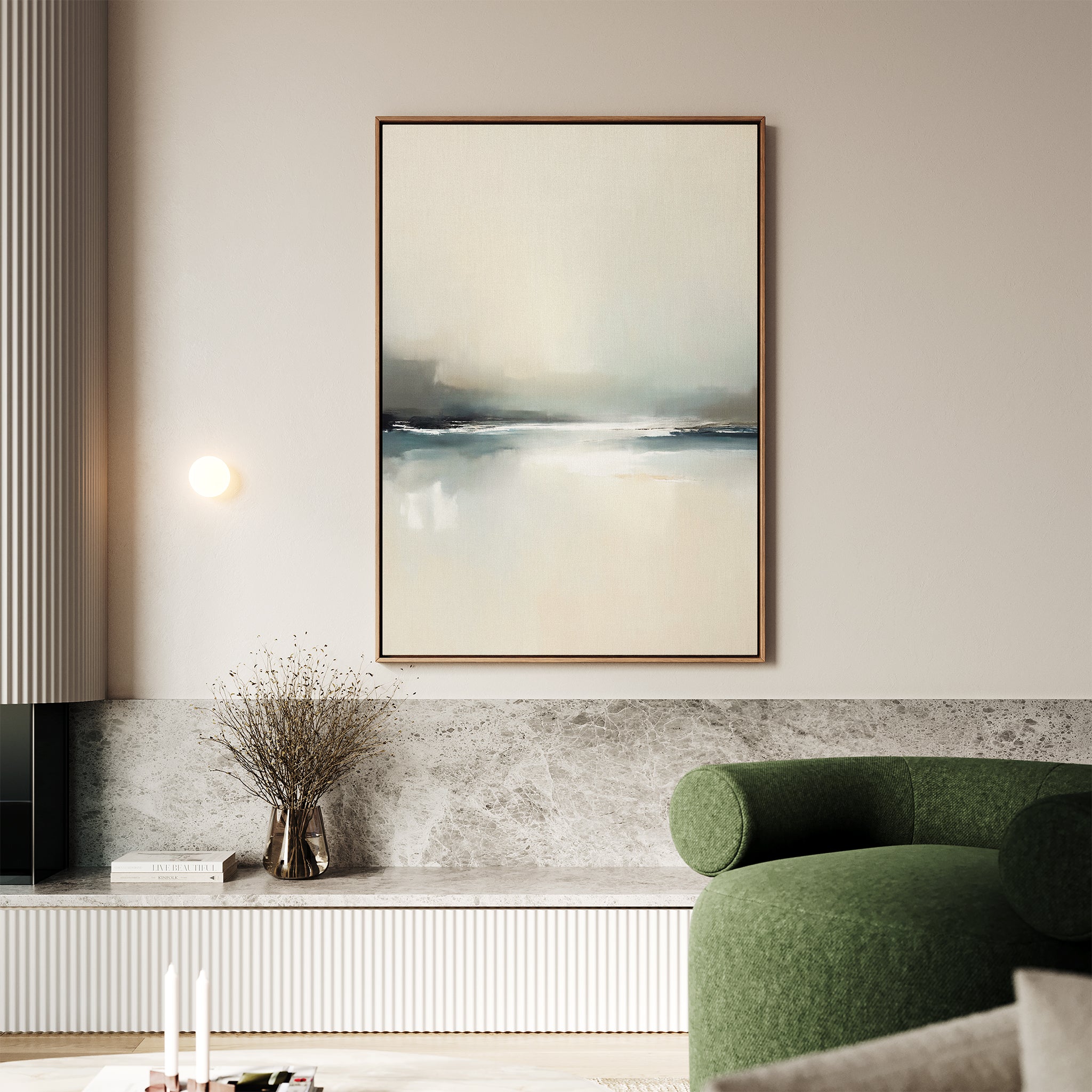 A minimalist living room features the Veiled Estuary Canvas Art - Vertical on the wall, a small round light fixture, a vase with dried branches on a marble ledge, and a green curved upholstered sofa in the foreground.