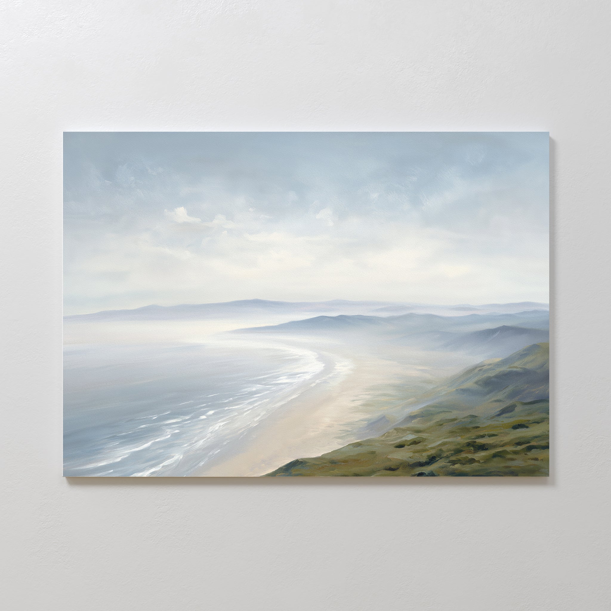 The Veiled Shores Canvas Art - Horizontal captures a serene coastal landscape with gentle waves, misty hills, and distant mountains beneath a cloudy sky in muted blues, greens, and sandy tones—ideal wall decor.