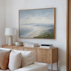 A minimalist living room featuring a wooden sideboard, books, a white lamp, and the Veiled Shores Canvas Art - Horizontal above, creating serene coastal Nordic Park vibes.