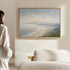 A woman in a white outfit stands in a minimalist, sunlit room, admiring the Veiled Shores Canvas Art - Horizontal displayed above a beige sofa.