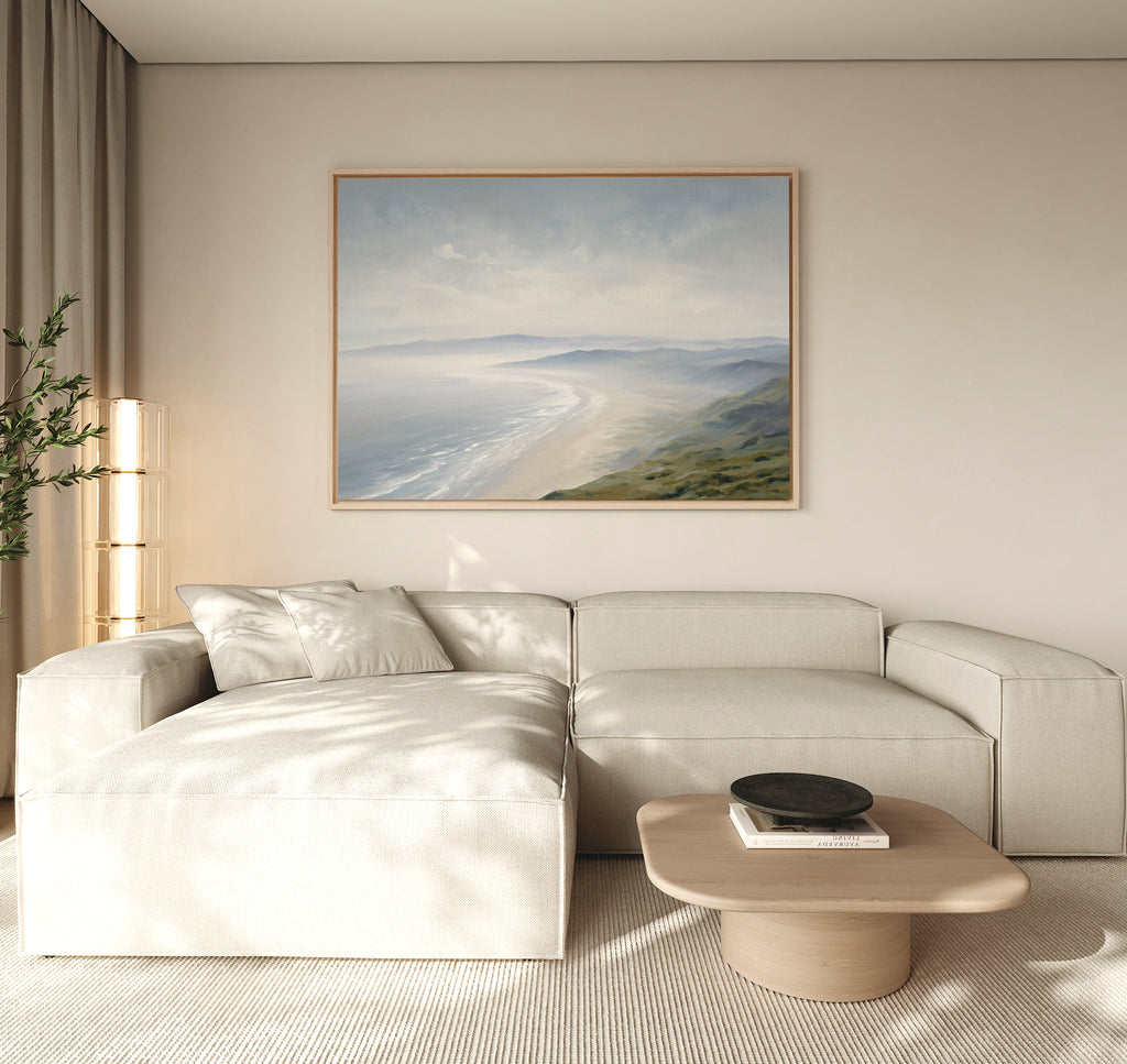A modern living room with a light beige sectional sofa, low wooden coffee table with a black bowl, neutral walls, and Veiled Shores Canvas Art - Horizontal hanging above the sofa. Natural light enters from the left.