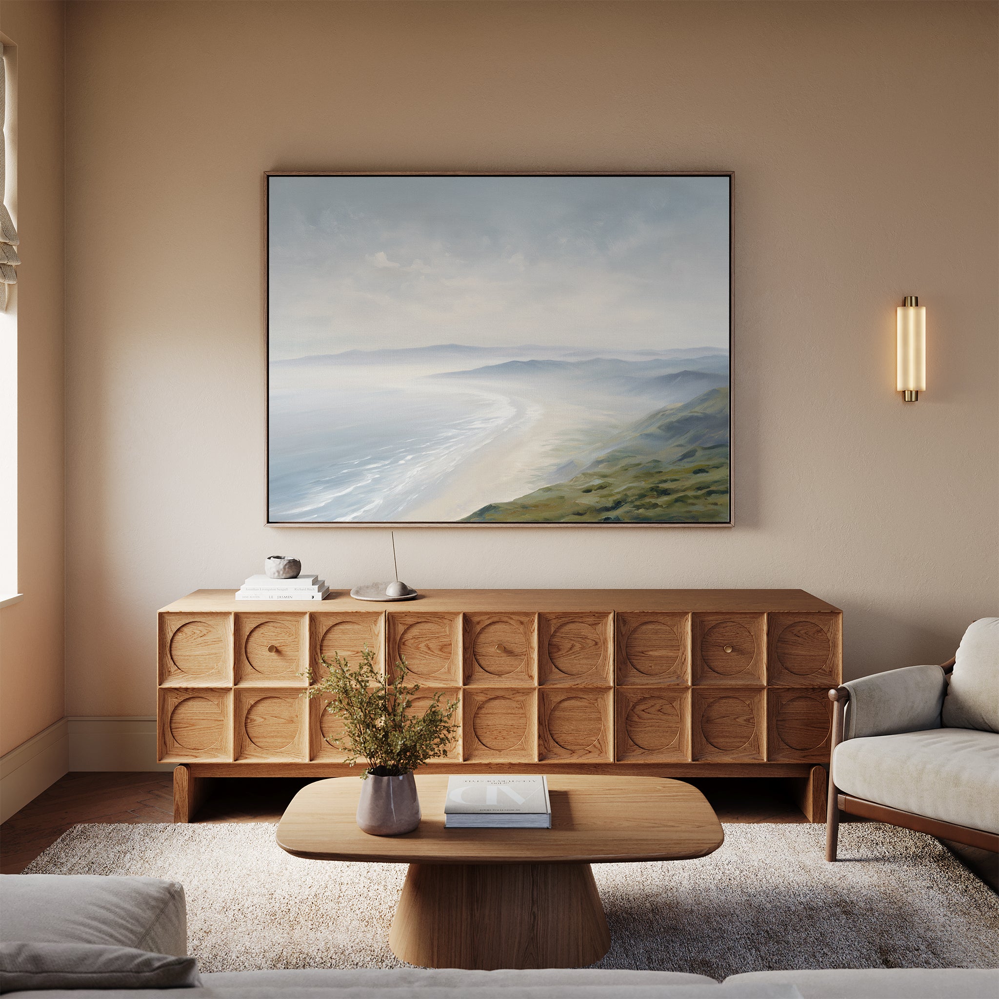 A cozy living room features a light wood sideboard, coffee table, and beige sofa. Above the sideboard hangs the Veiled Shores Canvas Art - Horizontal, depicting a serene coastal scene. A small lamp and vase add to the Nordic Park-inspired decor.