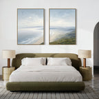 A modern bedroom with an olive green upholstered bed, white bedding, matching nightstands with beige lamps, and the Veiled Shores - Set of 2 coastal landscape canvas art hanging above the bed.