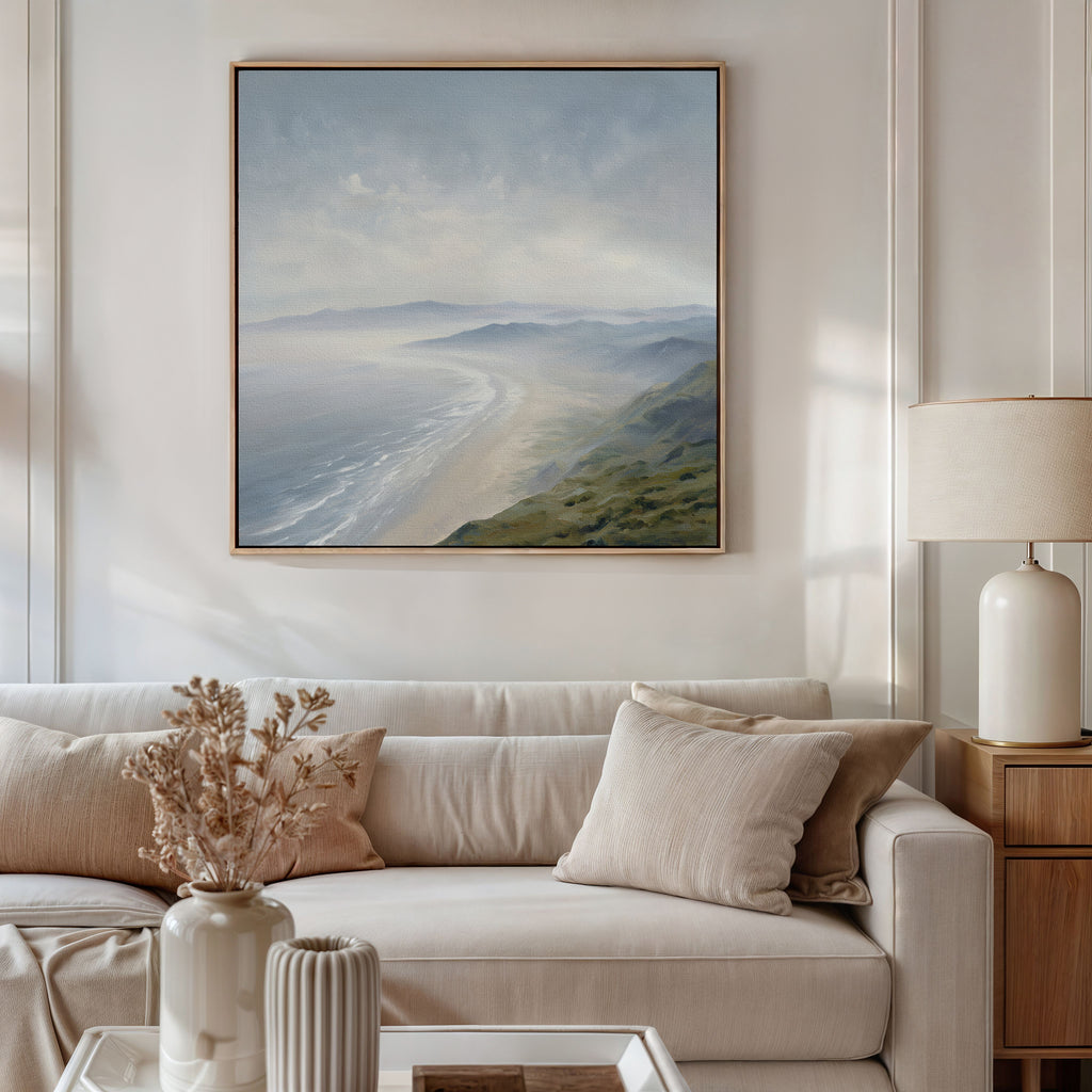 A cozy living room with a beige sofa, neutral cushions, a side table with a lamp, and a vase of dried flowers. Above the sofa, the Veiled Shores Canvas Art - Square adds serene Nordic Park vibes with its coastal landscape print.