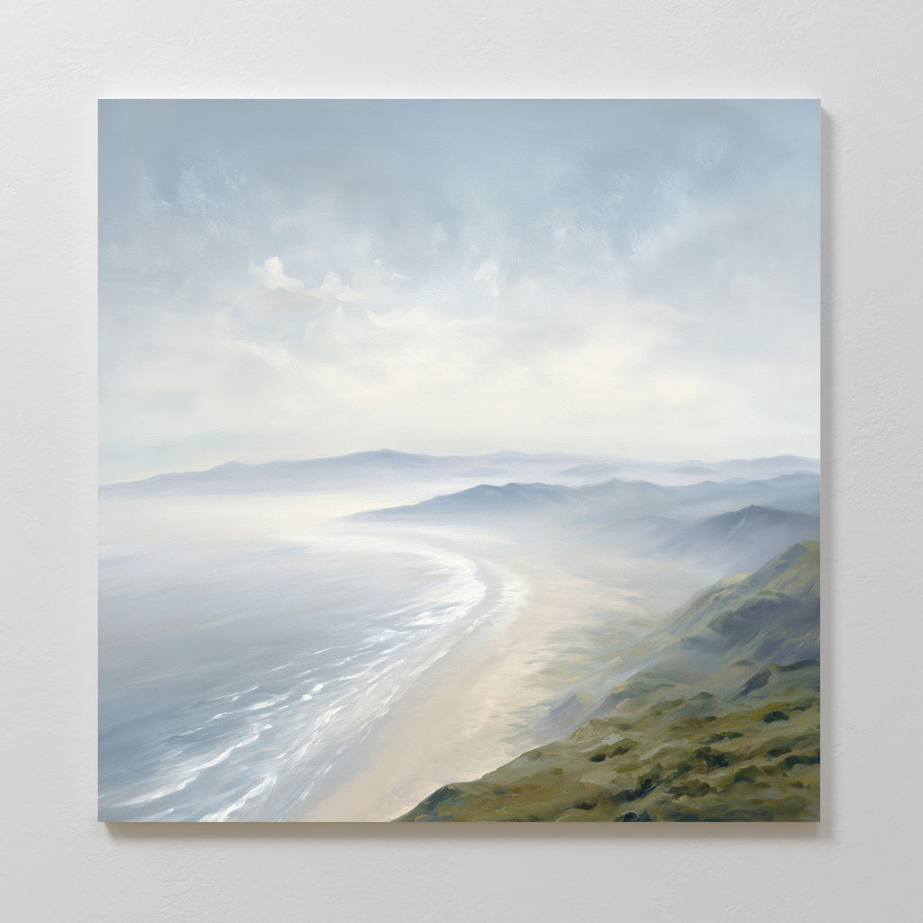 The "Veiled Shores Canvas Art - Square" showcases a misty coastal landscape with rolling hills and a sandy shoreline, soft blue-gray skies, and gentle waves, creating a peaceful atmosphere—ideal as coastal wall art.