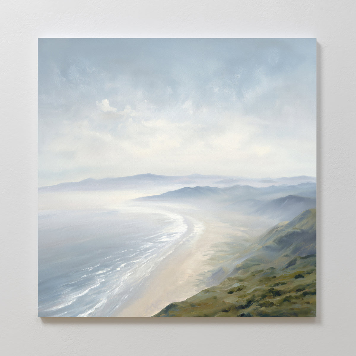 The "Veiled Shores Canvas Art - Square" showcases a misty coastal landscape with rolling hills and a sandy shoreline, soft blue-gray skies, and gentle waves, creating a peaceful atmosphere—ideal as coastal wall art.