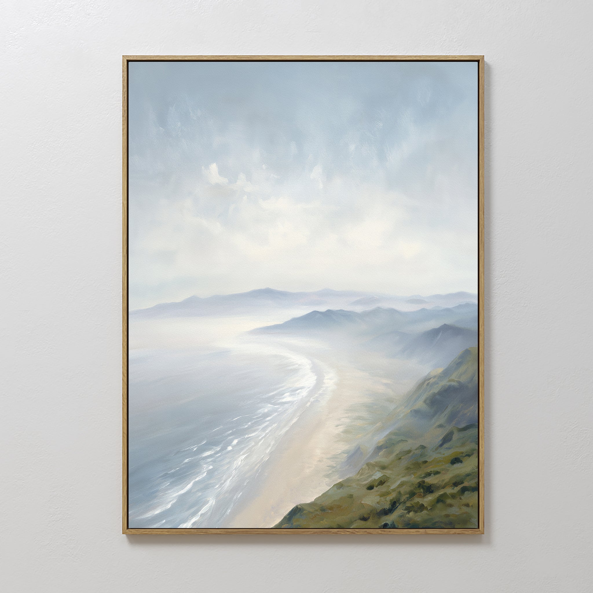 The Veiled Shores Canvas Art - Vertical features a framed coastal landscape of misty mountains, sandy beach, and waves under a cloudy sky, adding tranquil elegance when displayed against a plain white wall.