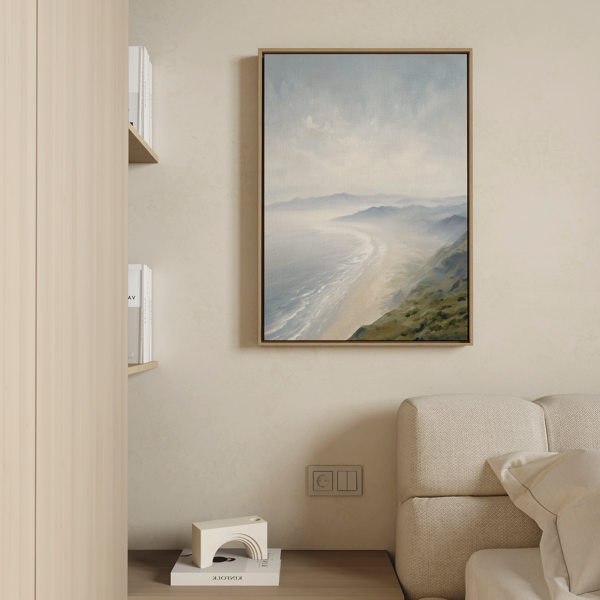 The Veiled Shores Canvas Art - Vertical hangs on a beige wall above a light sofa in a modern, minimalist living room, adding tranquil mountain and ocean vibes to the serene space.