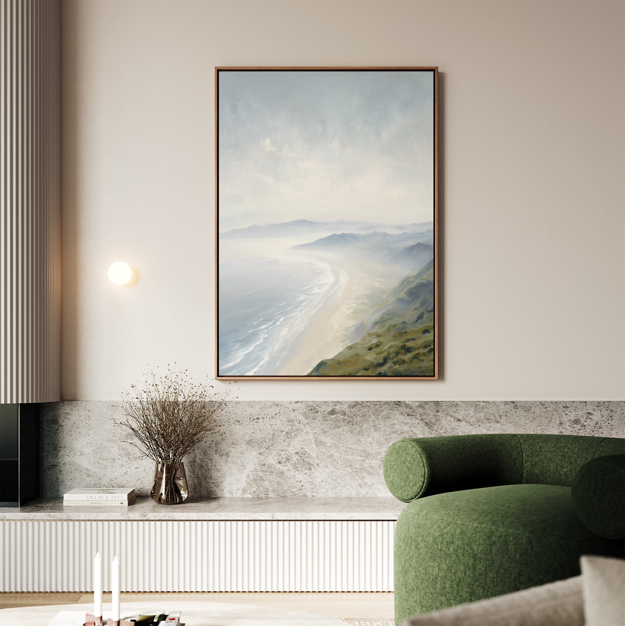A modern living room displays the Veiled Shores Canvas Art - Vertical above a marble bench, paired with a round green armchair and a small vase of dried branches below the artwork.