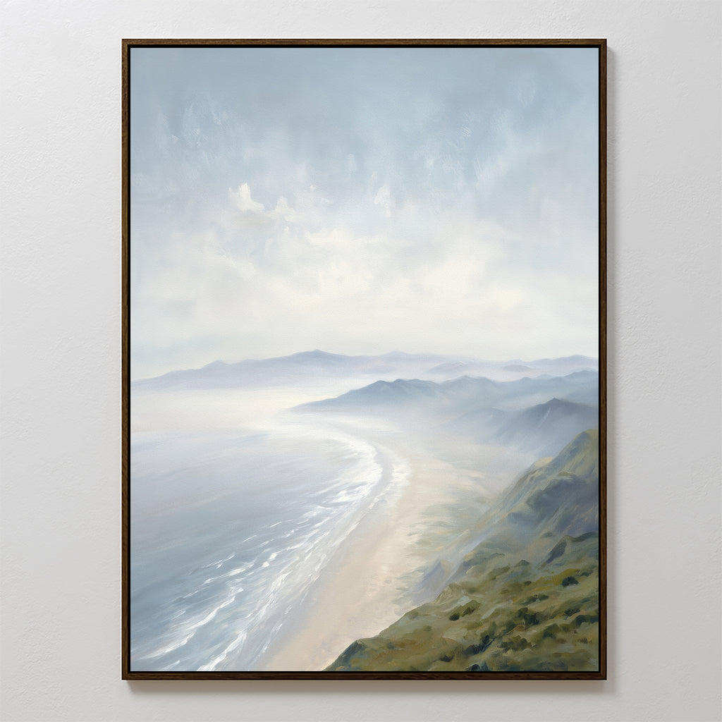 The Veiled Shores Canvas Art - Vertical features a tranquil, hazy coastline with gentle waves, sandy beach, and green hills beneath a cloudy sky. This framed coastal landscape is displayed on a white wall from an elevated perspective.