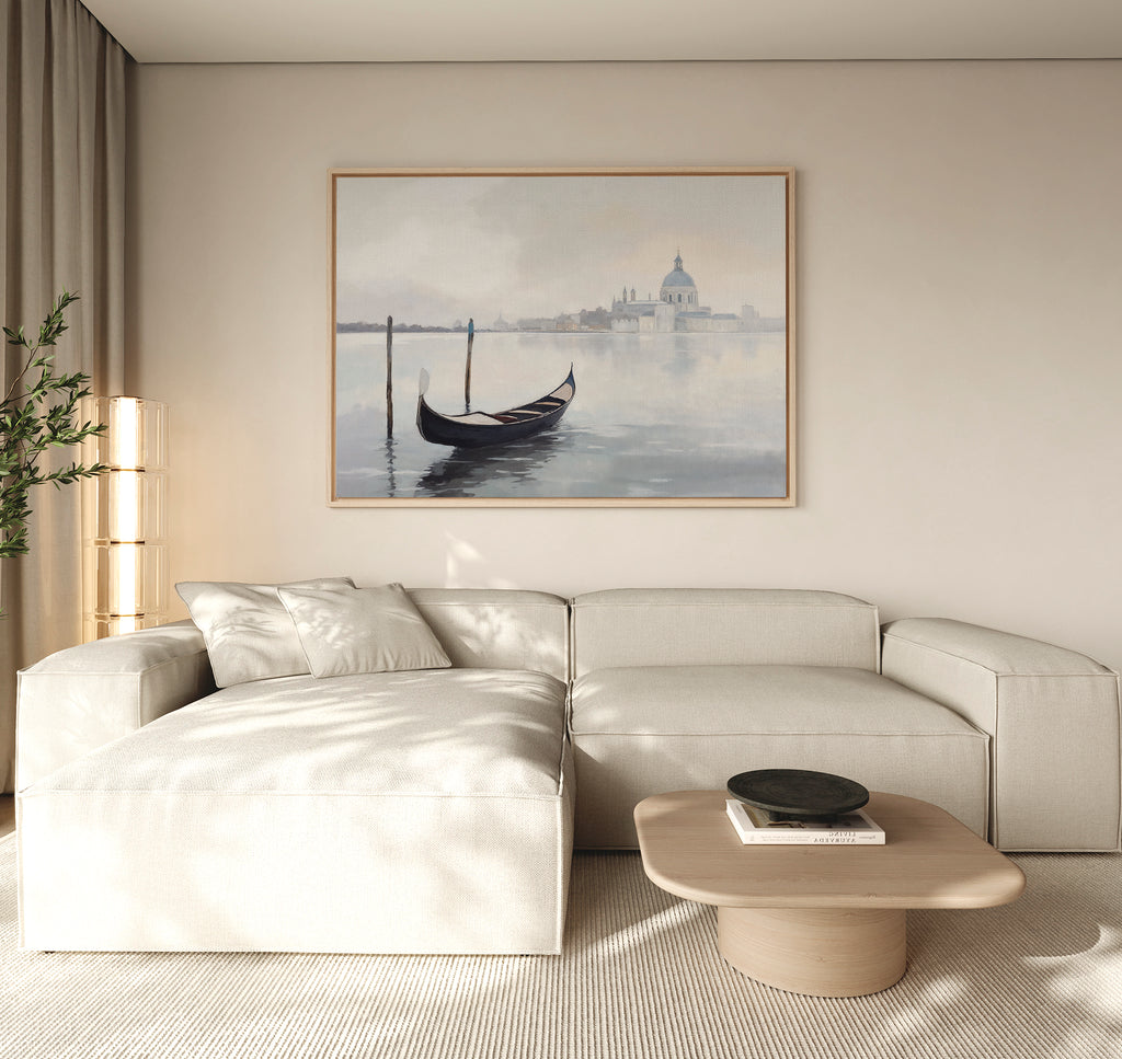 A minimalist living room features a cream sectional, light wood coffee table, and the Venetian Stillness Canvas Art - Horizontal displayed above the sofa. Neutral tones and soft natural lighting complete the serene atmosphere.