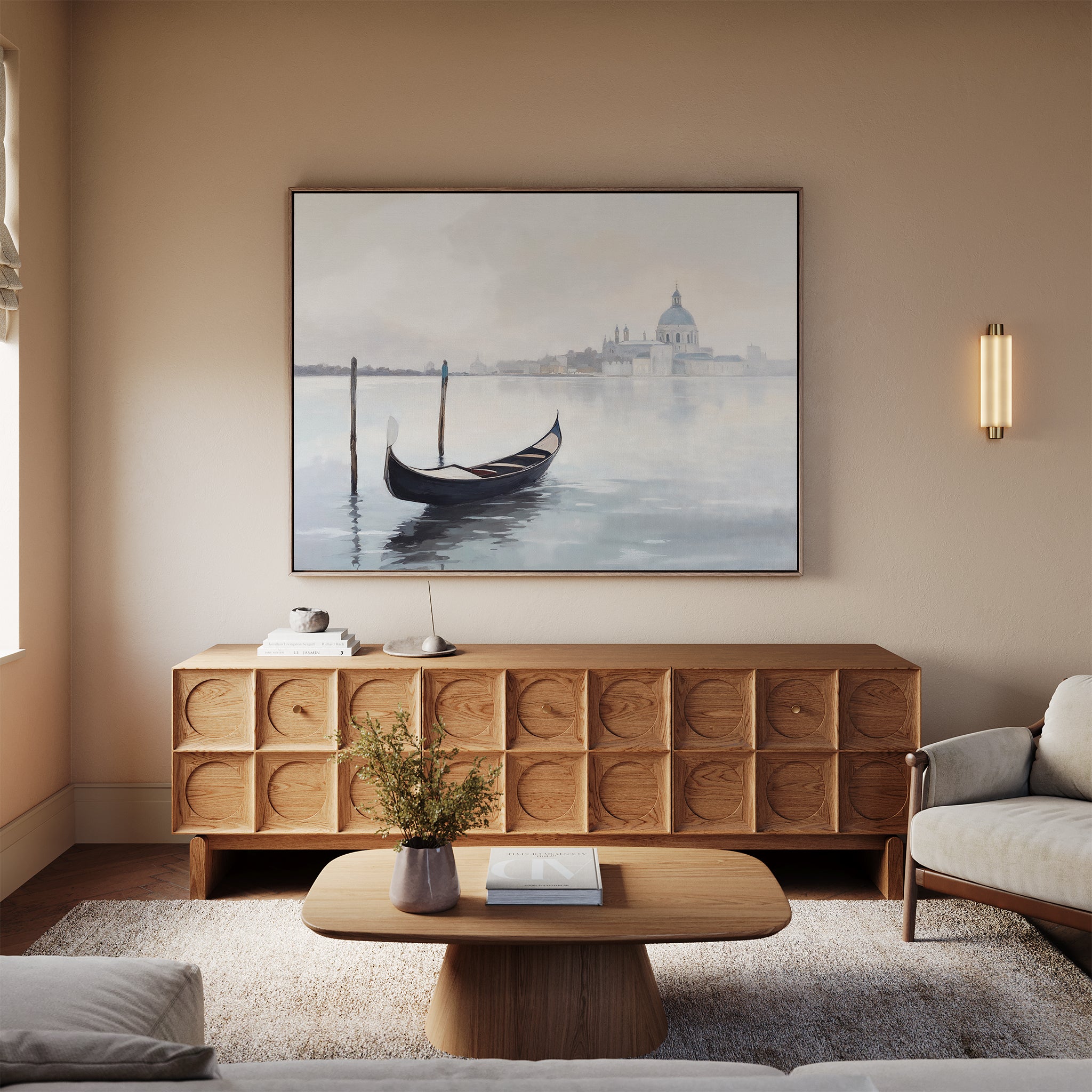 A modern living room with neutral walls, a wooden sideboard, coffee table, sofa, and the Venetian Stillness Canvas Art - Horizontal featuring a gondola on the water with buildings in the background above the sideboard.