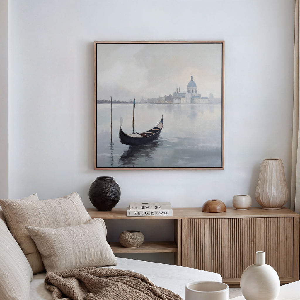 A cozy, neutral-toned living room features a light sofa and wooden sideboard, highlighted by the "Venetian Stillness Canvas Art - Square," which adds European charm with its gondola and distant cityscape motif.