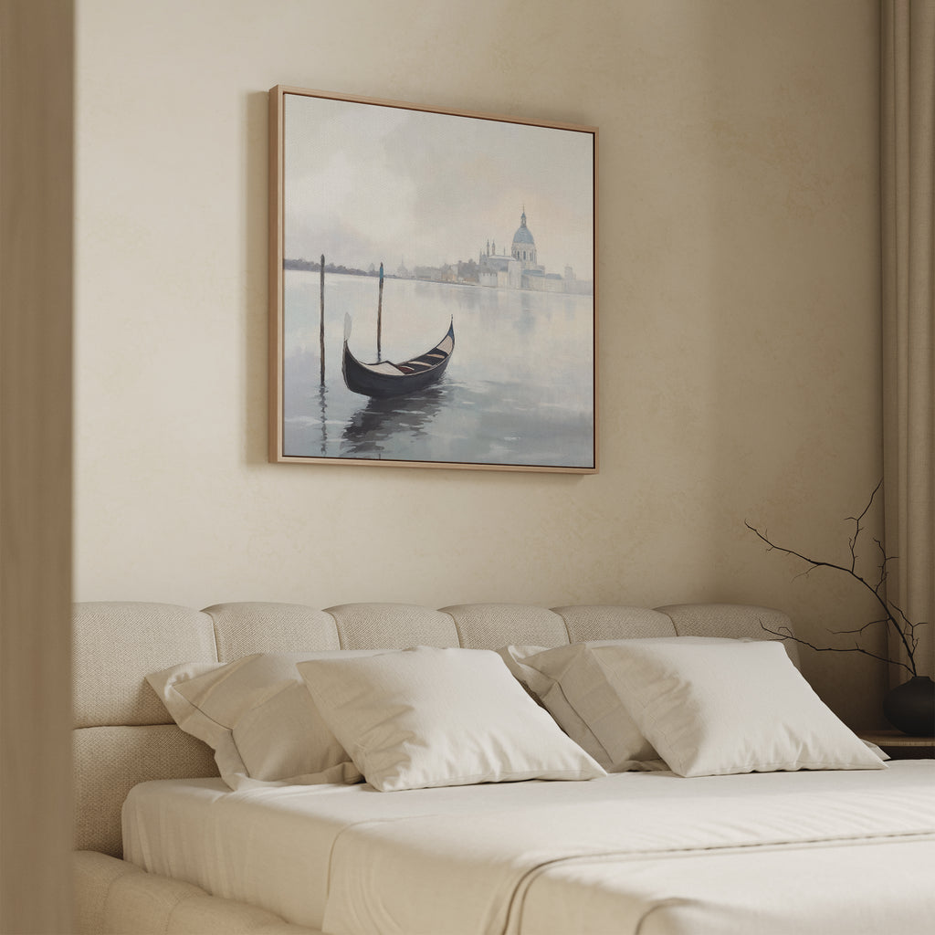 A minimal, beige bedroom with a cushioned headboard, white pillows, and the Venetian Stillness Canvas Art - Square of a gondola on calm water above the bed. A bare branch in a vase brings European charm to the nightstand.