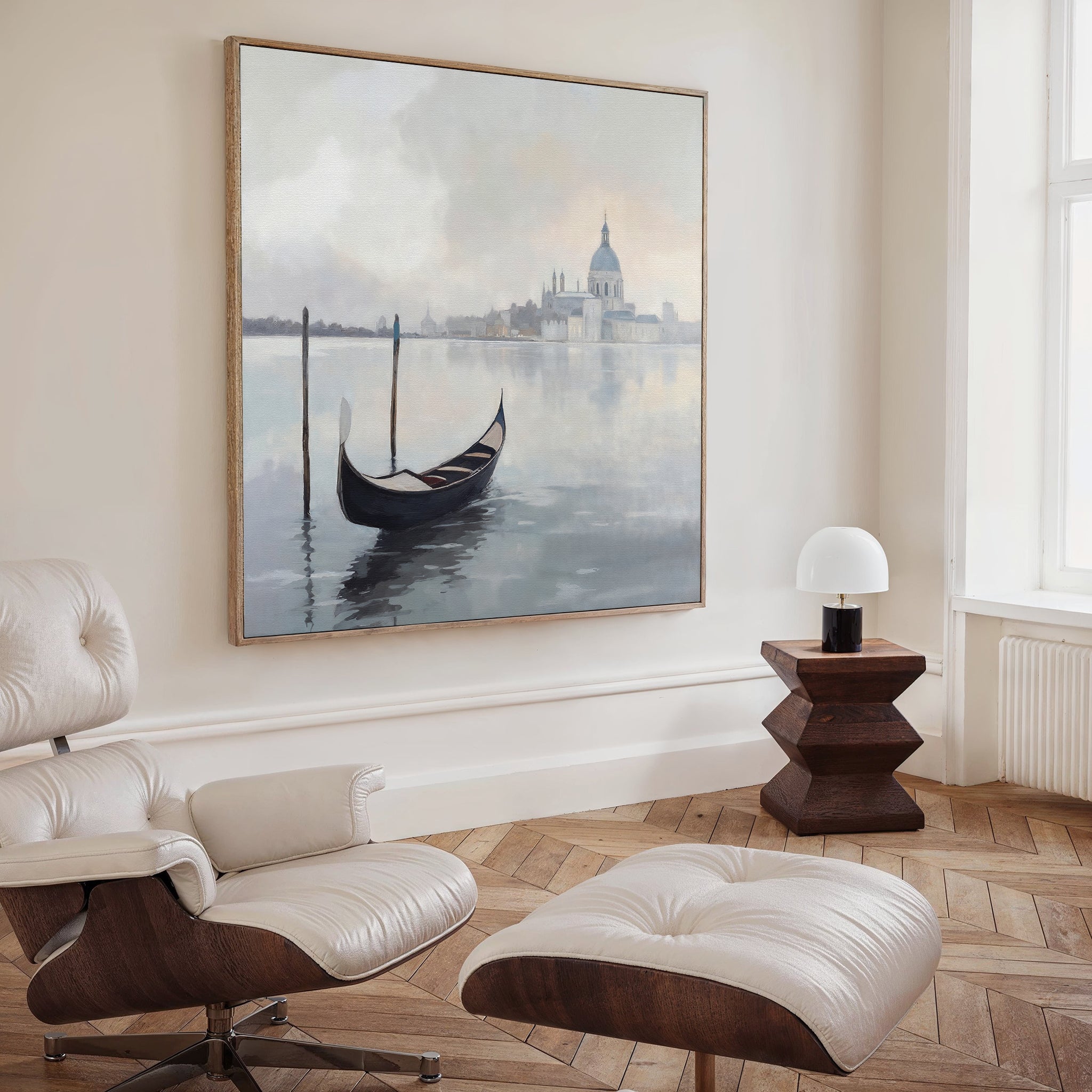 A modern living room featuring a white lounge chair, dark wood side table, and the "Venetian Stillness Canvas Art - Square" brings unmistakable European charm to the serene space.