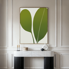 A modern console table with a white marble top sits against a beige paneled wall, adorned with candles and a white vase. Above it hangs the Verdant Duo Abstract Canvas Art, featuring two large green leaves for elegant living room decor.