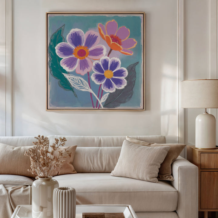 A modern living room with a white sofa, beige cushions, a wooden side table topped by a white lamp, and the Vibrant Petals Canvas Art - Square featuring purple and orange flowers hanging above the sofa.