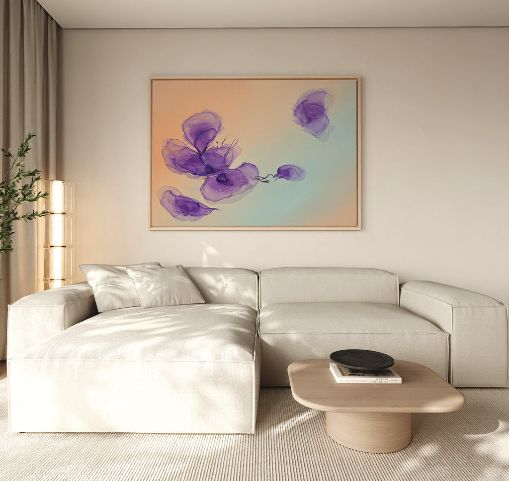 A modern living room with a light beige sectional, wooden coffee table, and the Violet Dreams Canvas Art - Horizontal featuring abstract purple flowers on a peach-blue gradient, displayed above the sofa.