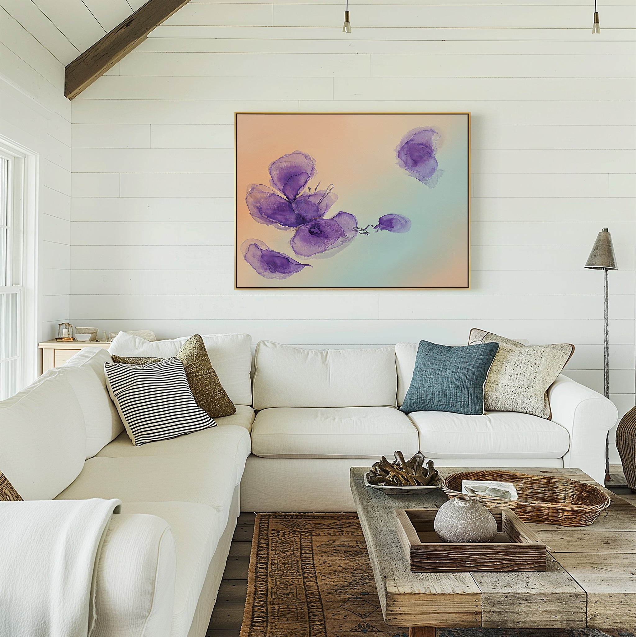 A bright, airy living room with a white sectional sofa, neutral and blue cushions, a rustic wooden coffee table, decorative accents, and the Violet Dreams Canvas Art - Horizontal featuring purple flowers on the wall.