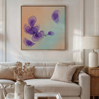 A modern living room features a white sofa with beige and white cushions, a side table with a lamp, and dried flowers. Above the sofa hangs the Violet Dreams Canvas Art - Square, showcasing purple watercolor flowers for an elegant touch.